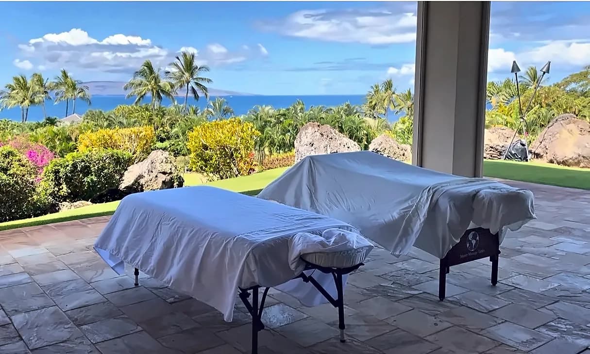 Two massage tables on a tropical patio with volcanic rock, bougainvillea, and ocean views